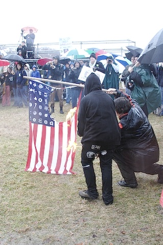 An altered American flag being burned during a protest.